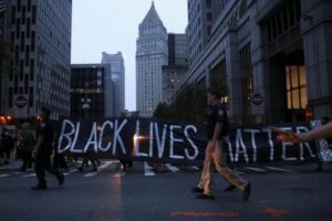 Policemen walk on the sidelines as protesters hold a sign which states "Black Lives Matter," during a march against police brutality in Manhattan, New York, U.S., July 9, 2016. REUTERS/Bria Webb